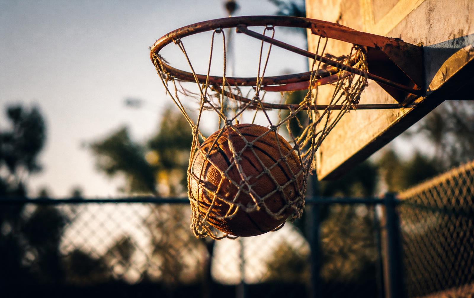 A basketball dropping through a worn net on an outdoor court at golden hour